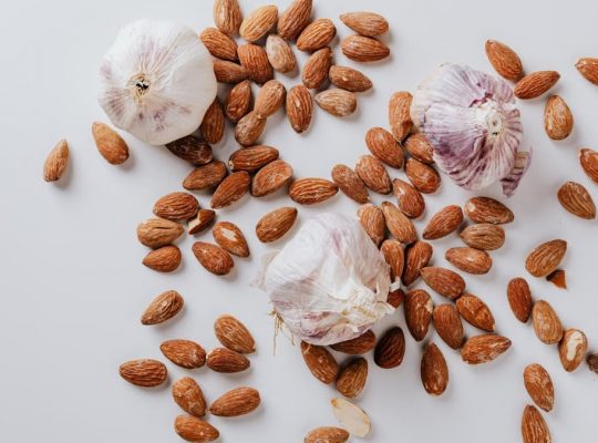 Top view of pile of raw partially peeled almonds and whole garlic bulbs with dry husk on white surface