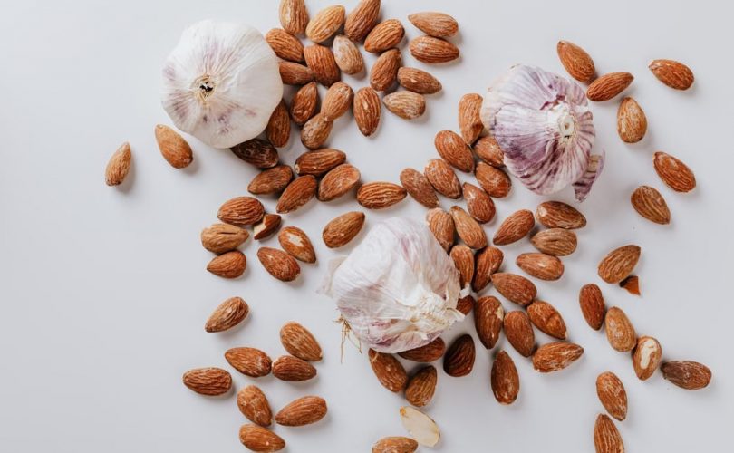 Top view of pile of raw partially peeled almonds and whole garlic bulbs with dry husk on white surface